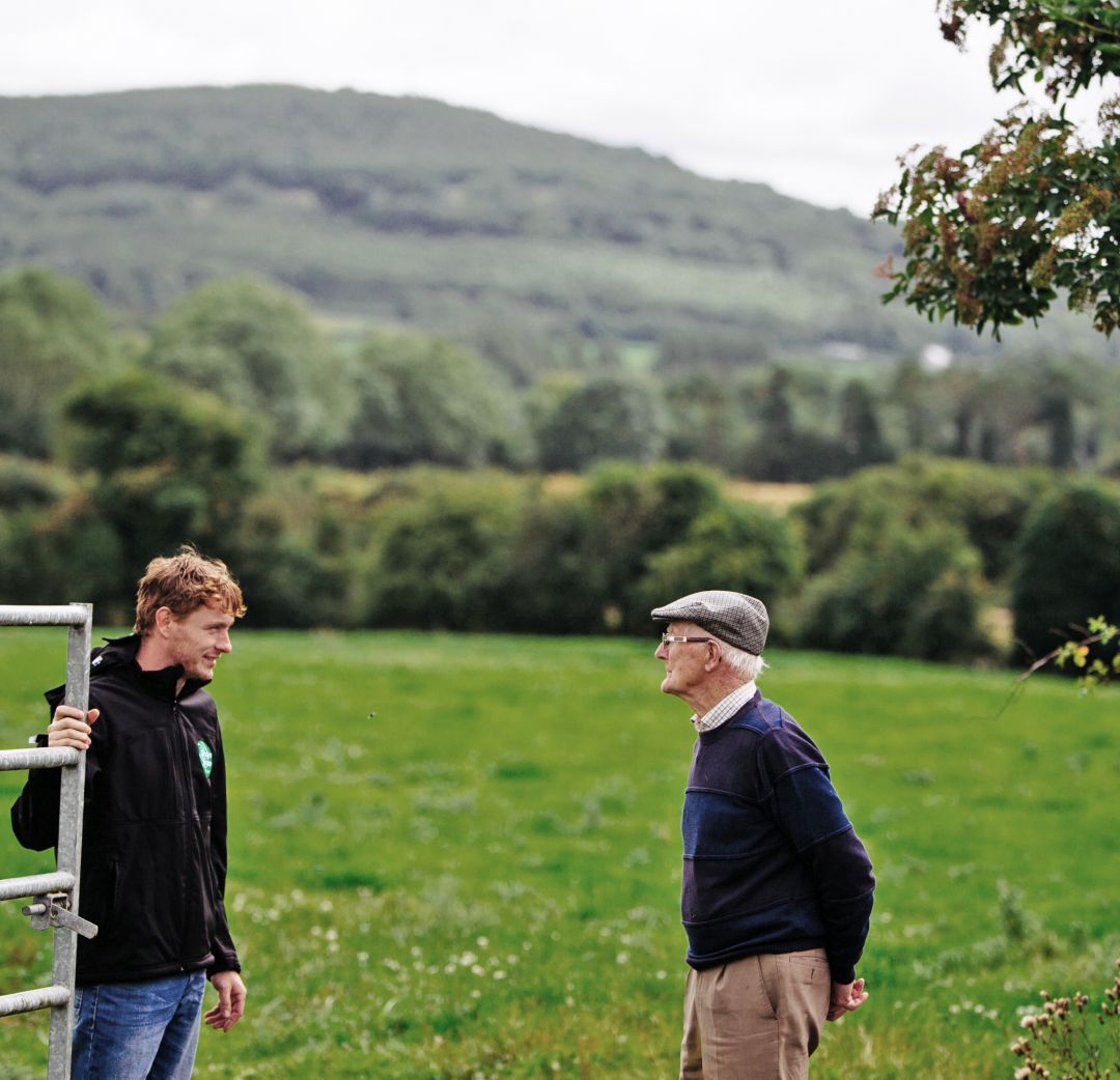 Un jeune et un ancien agriculteur discutent dans un pâturage irlandais avec des collines en arrière-plan